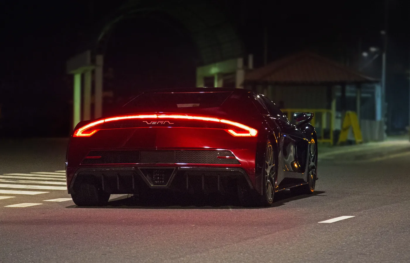 The VEGA from behind at night, its full-width tail light glowing